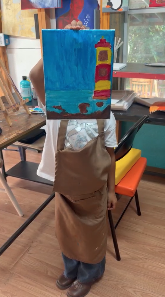 Child holding up a lighthouse painting